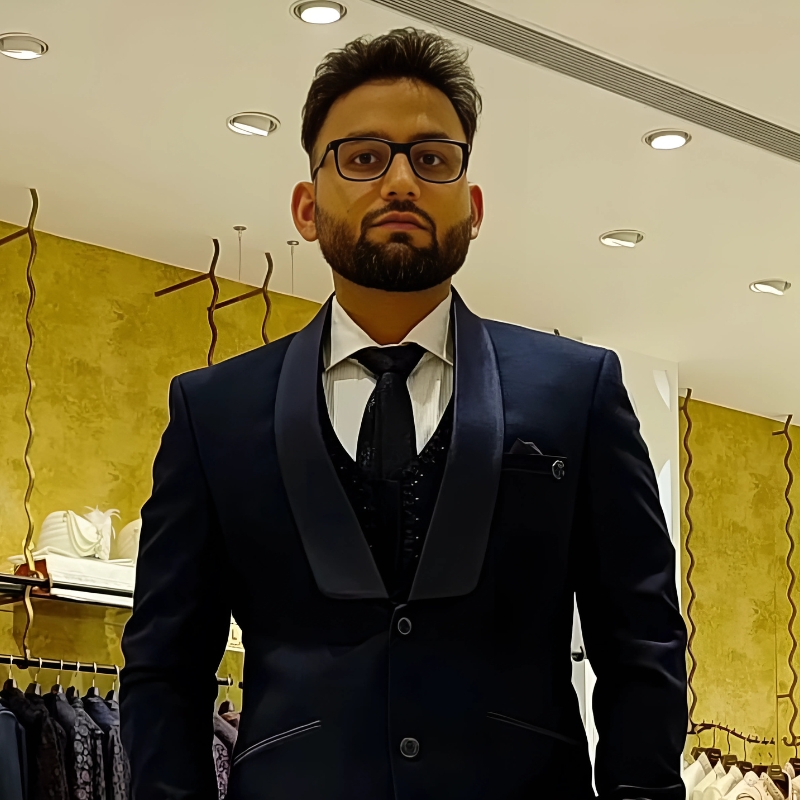 A man dressed in a formal suit with glasses, looking confidently at the camera.