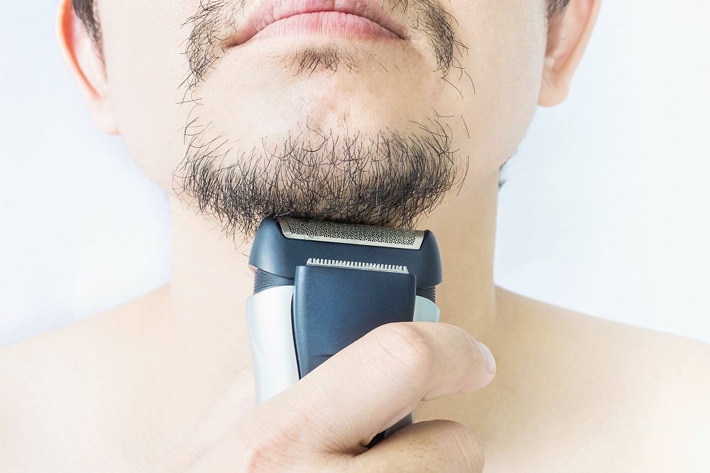 Close-up of a man using an electric shaver to trim his facial hair.